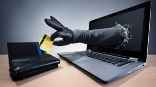 Mão "saindo" da tela de computador e pegando um cartão de crédito numa carteira