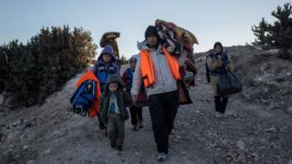 An Afghan refugee family walk with their belongings and lifejackets to a campsite to wait for a boat to leave Turkey