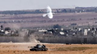 9月4日、トルコ南部キリス県エルベイリから撮影したシリア国境向こうのトルコ軍戦車と、その近くを飛ぶ鳥