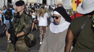 an armed soldier in full camouflage walking past a woman in a nun's habit, 15 August 2016