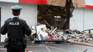 back of policeman in foreground, exploded ATM unit in background