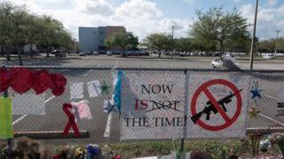 A sign at floral tribute at Parkland school reads "Now is the time" with a symbol of a gun crossed out