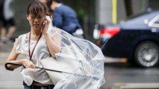 A woman crosses a street holding a damaged umbrella caused by strong wind generated generated by typhoon Mindulle in Tokyo, Japan, 22 August 2016.