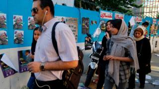 Iranians walk by a wall plastered with election posters on a street in the capital Tehran on 17 May 2017