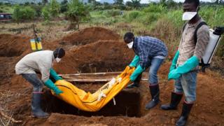 Volunteers in protective suit burry the body of a person who died from Ebola in Waterloo, some 30 kilometers southeast of Freetown, on October 7, 2014.