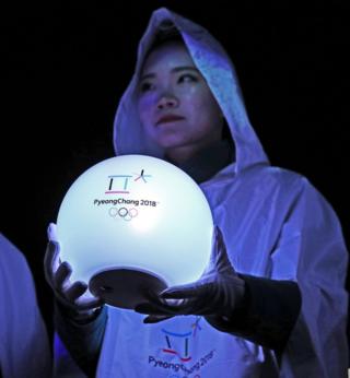 A woman holds a glowing ball with the Pyeongchang Olympics 2018 on