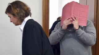 Nurse is led into a court handcuffed hiding behind a folder