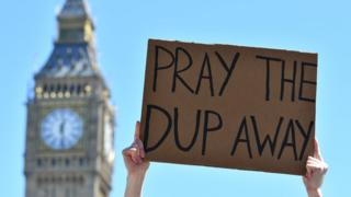 A protester holds up a placard as they protest in Parliament Square in front of the Houses of Parliament in central London on 10 June 2017 against the Democratic Unionist Party (DUP)
