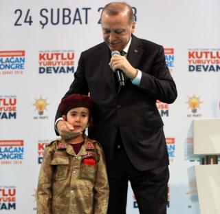 Turkish President Recep Tayyip Erdogan speaks alongside a girl dressed as a Turkish soldier