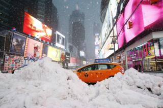 A taxi drives past piles of snow as a storm sweeps through Times Square in New York on 14 March 2017.