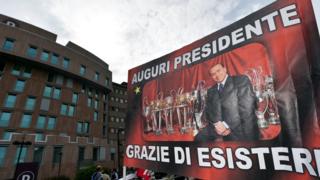 "All the best, president - thanks for being there", a banner reads outside the hospital in Milan where Mr Berlusconi underwent the operation