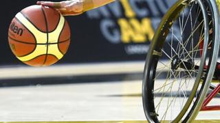 A cropped image showing a basketball and the wheel of a wheelchair