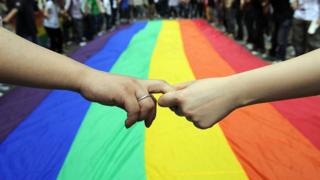 Hands being held in front of giant rainbow flag, Hong Kong