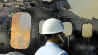 Una persona de equipos de rescate frente al fuselaje de un avión quemado