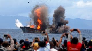 People take pictures of a burning ship as the government destroyed foreign boats at Morela village in Ambon island