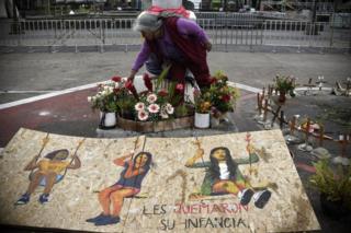 Mujer deja flores ante un cartel dedicado a las víctimas de la tragedia del Hogar Seguro Virgen de la Asunción de Guatemala.