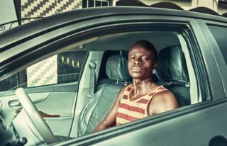 Kwame sits in his car