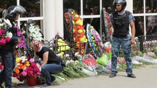 A woman places flowers as Interior Ministry members stand guard outside the firearms shop, which was a target of a recent suspected Islamist militant attack, during the funeral of salesman Andrey Maksimenko in Aktobe, Kazakhstan, June 8, 2016.