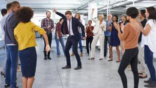Una persona bailando en medio de un círculo de colegas en la oficina
