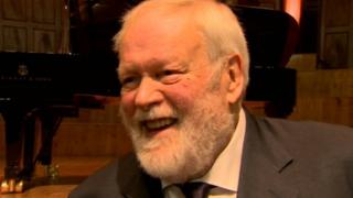 Michael Longley sitting in front of a piano