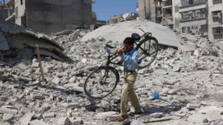 Hombre lleva una bicicleta en sus hombros tras un bombardeo en Alepo.