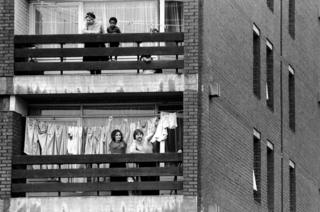 Local residents are pictured watching the gather. Two National Front supporters cheer and clap from the balcony of their tower block flat.