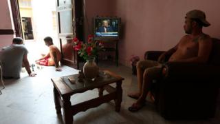 Un cubano ve el discurso de Trump desde el televisor de su casa mientras dos jóvenes juegan ajedrez en el portal de la casa.