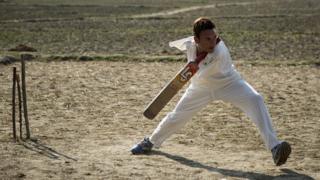 Amir holds the cricket bat between his neck and shoulder
