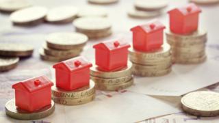 Miniature red houses resting on pound coin stacks