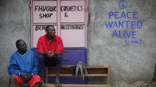 Men sit in front of a wall with a message of peace painted recently by local street artist Solomon Muyundo in Kibera, Nairobi