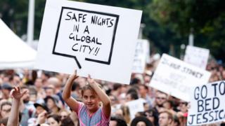 A protest placard reads: "Safe Nights In a Global City"