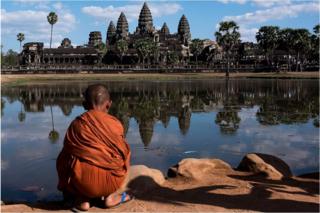 A young monk sits in front of a lack in front of the Angkor Wat temple on 1 January 2016, near Siem Riep, Cambodia.