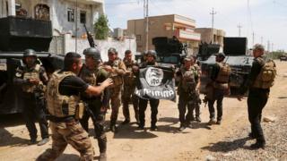 Iraqi troops hold Islamic State flag upside down inside town of Hit on 13 April 2016
