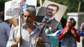 A Syrian man holding up portraits of President Bashar al-Assad and his Russian counterpart Valdimir Putin (L) joins several hundred people who gathered near the Russian embassy in Damascus to express their support for Moscow's air war in Syria