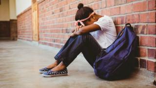 Adolescente sentada ao lado de uma mochila