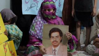 Imdad Ali's wife, her face mostly covered, holds a photo of her husband