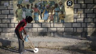 A boy playing with a homemade toy walks past an Oxfam sign in Port-au-Prince, Haiti,