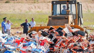 A bulldozer driving over boxes of peaches