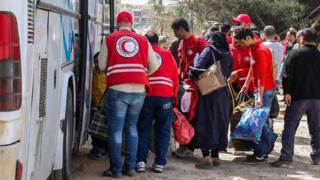 Syrian Arab Red Crescent workers help civilians being evacuated from the rebel-held town of Harasta, in the Eastern Ghouta, on to buses (22 March 2018)