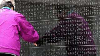 A woman in the city of Sendai touches the names of her relatives on a cenotaph on March 11, 2017, the sixth anniversary of the earthquake, tsunami and nuclear disasters in northeastern Japan.