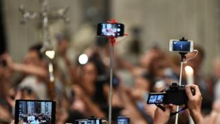 Teléfonos en palos de selfies tomando fotos de una cruz