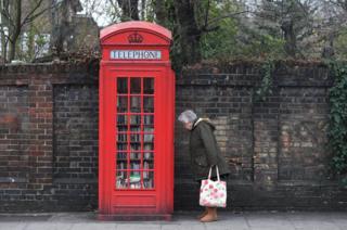 A woman looks at books in a decommissioned red telephone box in London