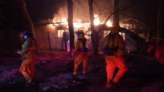 Firefighters investigate a burning house, as the Thomas wildfire continues to burn in Carpinteria, California, 10 December 2017