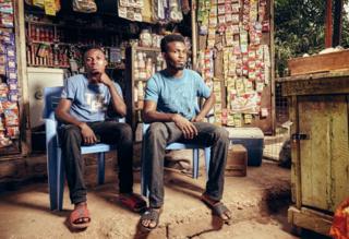 Two men sit outside a stall