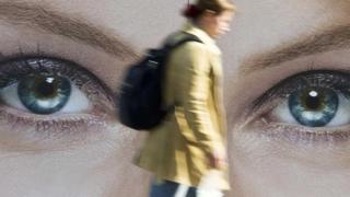 Una persona caminando frente a una imagen de unos ojos gigantes