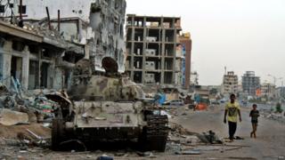 Young Yemenis walk past a tank destroyed in clashes between Houthi rebels and government forces in the port city of Aden - 19 August 2015