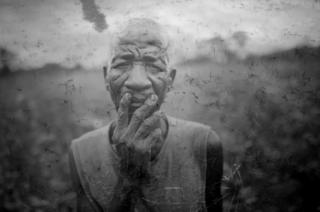 An elderly farmer stands in his field, overlaid onto an image of a puddle of murky water