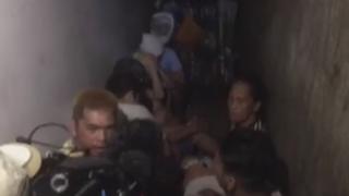 A screen grab from ABS-CBN news, showing people sat in a narrow and dark room