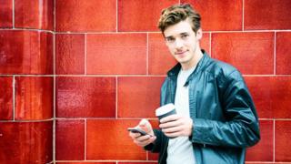 Un "millenial" sujeta su celular y un café.