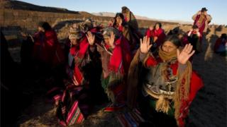 Aymara indigenous hold up their hands to receive the first rays of sunlight in a New Year's ritual in the ruins of the ancient city Tiwanaku, Bolivia, early Tuesday, June 21, 2016.